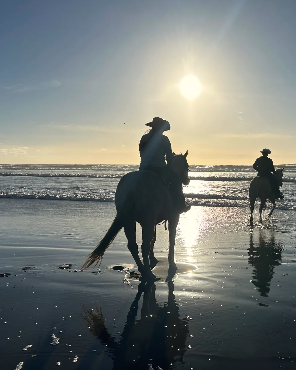 Two riders at the water's edge with the sun low over the Pacific