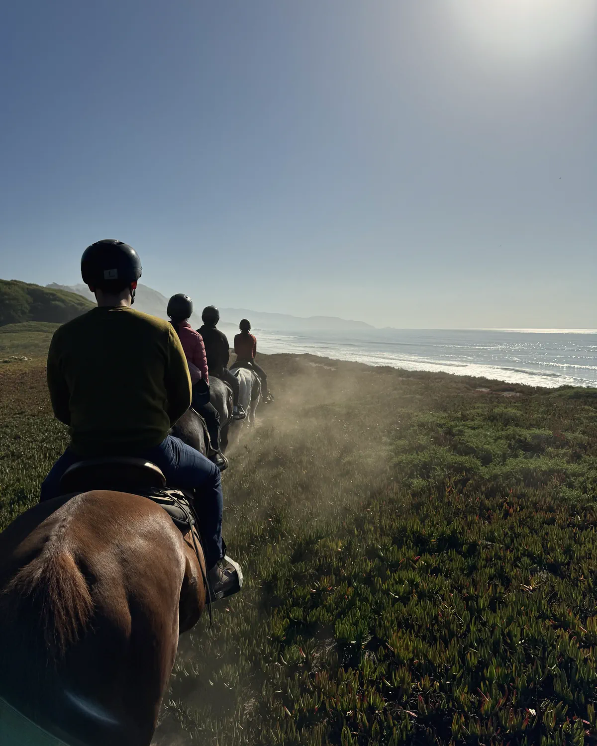 The view from the saddle behind a line of riders in helmets on the bluff trail above the surf